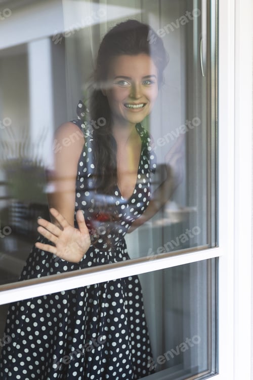 Preview: Gorgeous woman wearing beautiful dress with a polka dot pattern looking through the window