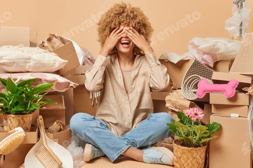 Preview: Happy woman covers eyes with hands waits for surprise sits crossed legs on floor wears shirt jeans
