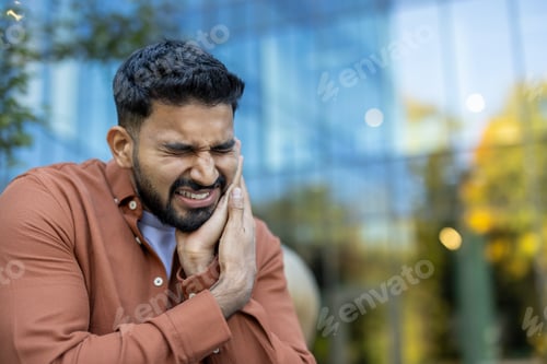 Preview: An Indian man is in agony with a severe toothache, holding his face in pain.