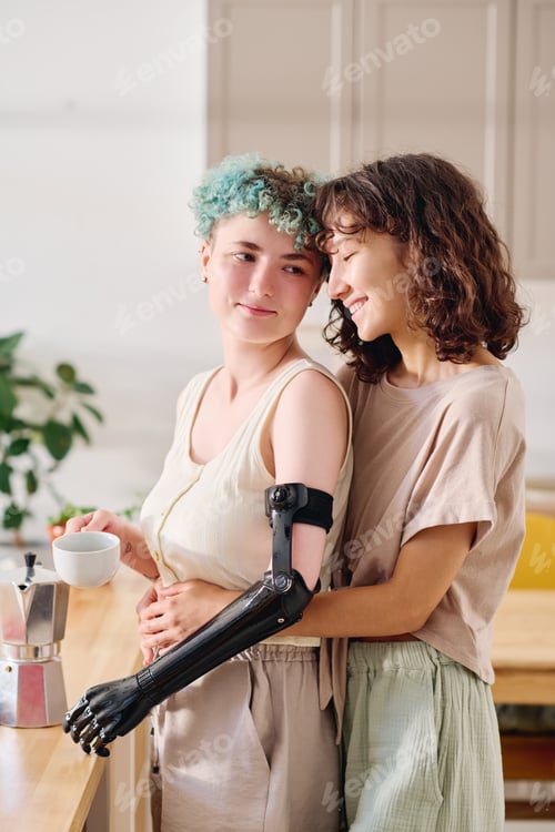 Preview: Young woman with disability holding cup of coffee and looking at happy girlfriend