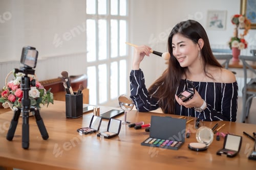 Preview: Young asian woman blogger with makeup cosmetics recording video clip online by smartphone at home. T