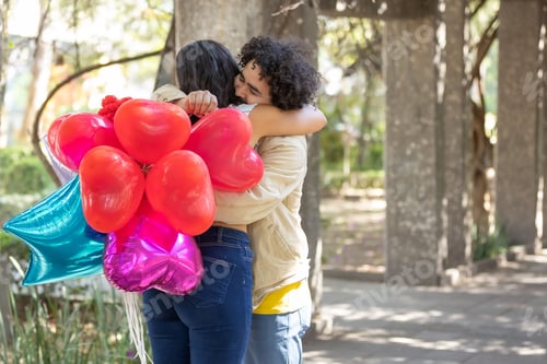 Preview: two women hugging in a park one holding red and one blue balloons