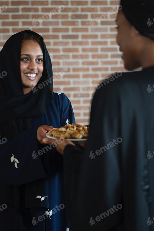 Preview: Muslim women wearing abayas gifting and sharing Arabic sweets during Ramadan