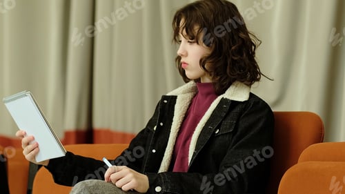 Preview: A girl playfully extends her notebook forward, her expression both focused and amusing. The photo