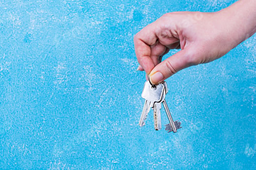 Preview: Female hand holding keys on blue background