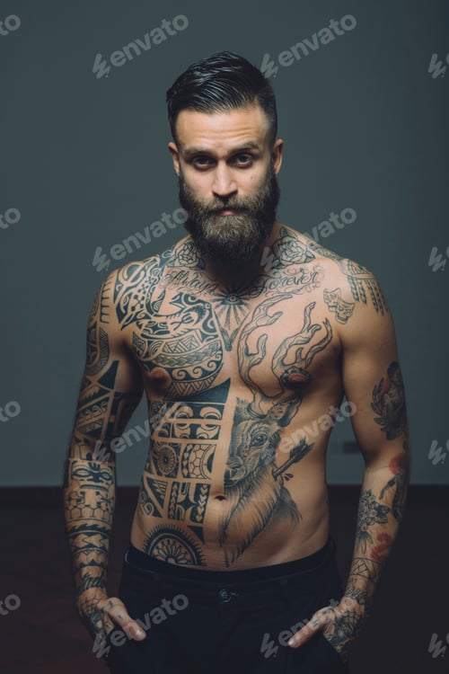Preview: Portrait of young man with beard, bare chest covered in tattoos