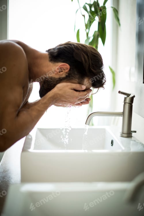 Preview: A man standing at a sink washing his face.