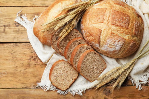 Preview: Different types of bread and wheat spikes on wooden table, flat lay. Space for text