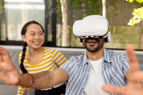 Preview: Using VR headset, man experiencing virtual reality while woman smiling nearby
