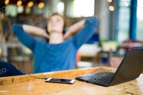 Preview: Laptop and smartphone on table with relaxing young man listening music in the background