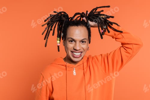 Preview: happy multiracial man touching dreadlocks on coral background