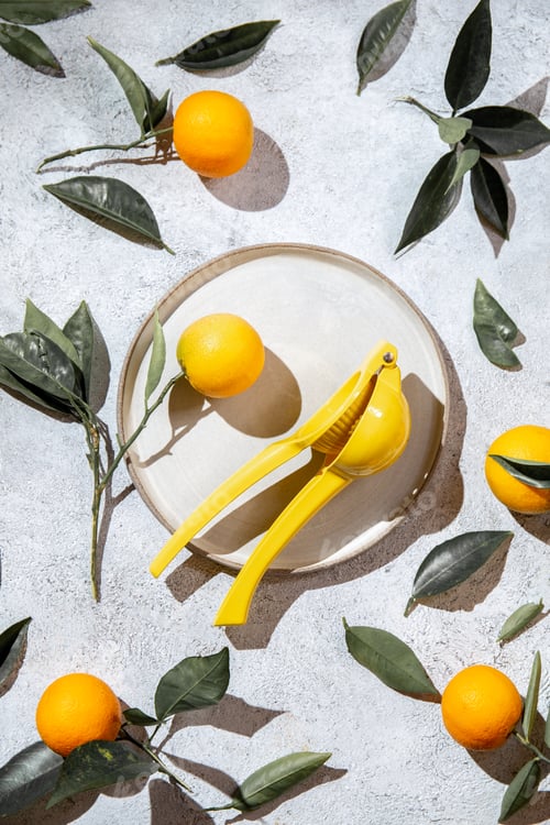 Preview: Whole oranges with orange tree leaves around plate and juicer top view, flat lay, summer and healthy