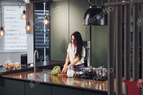 Preview: Young beautiful brunette in casual clothes preparing healthy food in kitchen at daytime