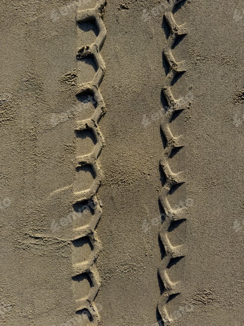 Preview: Close-up detail of a geometric pattern of tire tracks on sand