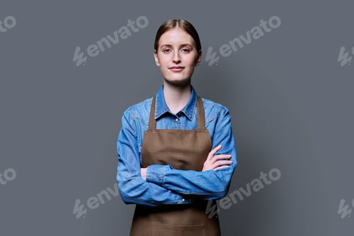 Preview: Portrait of young smiling confident woman in apron on grey background