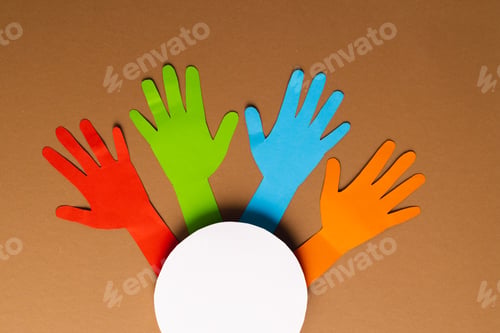 Preview: Paper cut out of multi coloured hands and white circle with copy space on brown background