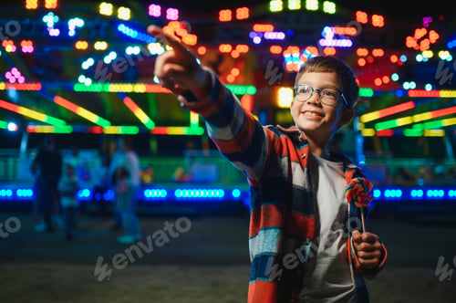 Preview: A cute caucasian boy eating a colorful lollipop standing against the background of a carousel