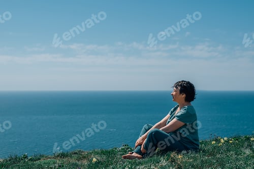 Preview: portrait of an adult woman sitting on the grass on a mountain against the background of the sky, sea