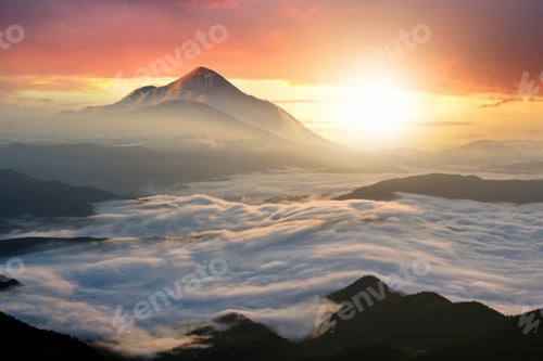 Preview: Sunset landscape with high peaks and foggy valley with thick white clouds under vibrant colorful
