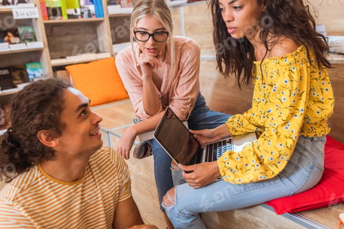 Preview: Three young students sitting on the floor in the library learning together.