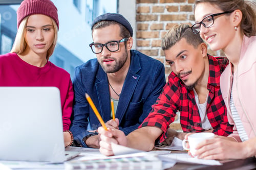 Preview: Four young stylish designers working at project in office looking on laptop