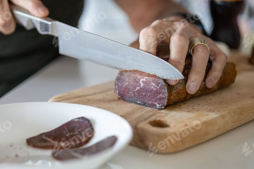 Preview: Chef preparing a meal in a kitchen, slicing pieces of pastirma on a wooden cutting board