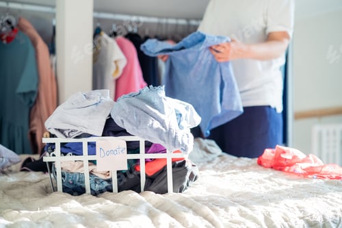 Preview: Woman cleaning and checking her wardrobe for donating clothes to a Charity shop. Reuse, second hand.