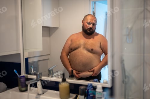 Preview: Oversize man touch sagging belly in front of mirror looks at reflection with disgust and displeasure