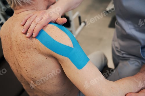 Preview: Physical therapist attaching kinesio tape to right shoulder of patient