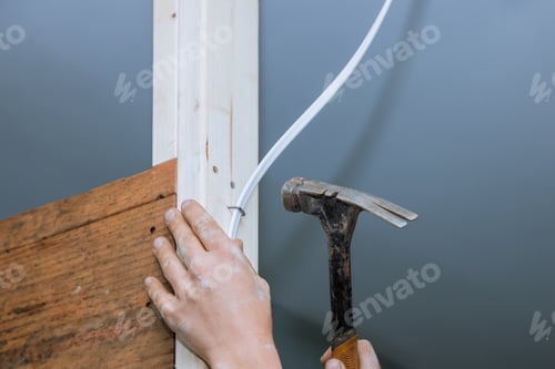 Preview: Contractor hand grips hammer while another adjusts electrical wiring against wooden framing in