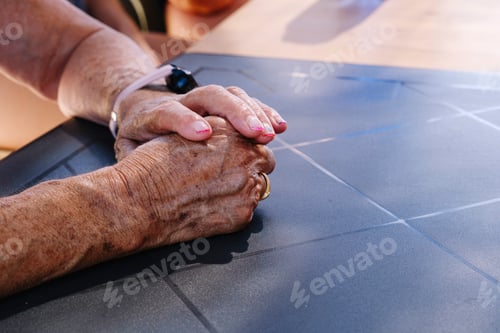 Preview: Intertwined hands of an older woman on the table.
