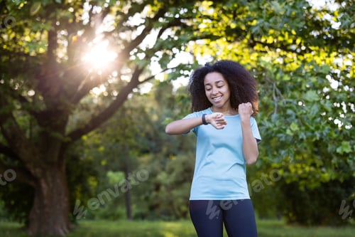Preview: African American female checking fitness tracker during outdoor workout in sunny park setting