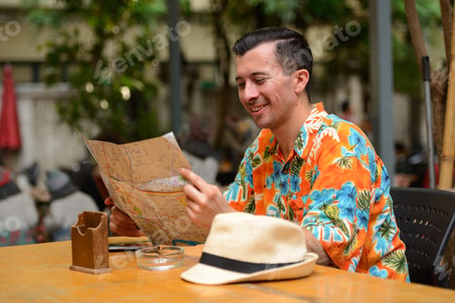 Preview: Happy young handsome tourist man reading map at the restaurant