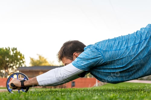 Preview: side view of unrecognizable caucasian with sportswear exercising with ab wheel on the grass