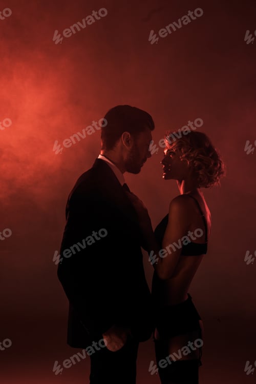 Preview: Attractive couple of young adults amorously looking at each other on red smoke background