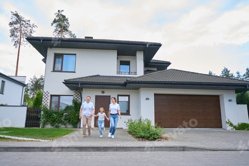 Preview: Family holding hands and running from new modern townhouse outdoors in warm day