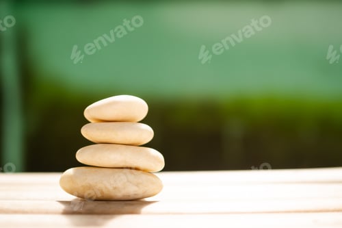 Preview: Stack pyramid stone zen pebbles on wooden with dark black and green blur background.