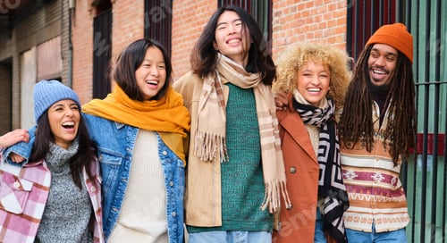 Preview: Group of five multiracial friends laughing and walking along the street.