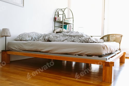 Preview: Unmade blanket on bed in bedroom with large bright window, sunbeam