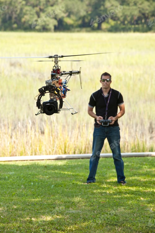 Preview: Man controlling helicopter drone, UAV with SLR camera attached.