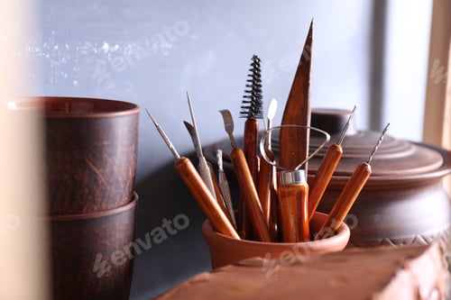 Preview: Set of different crafting tools and clay dishes on wooden rack in workshop, closeup