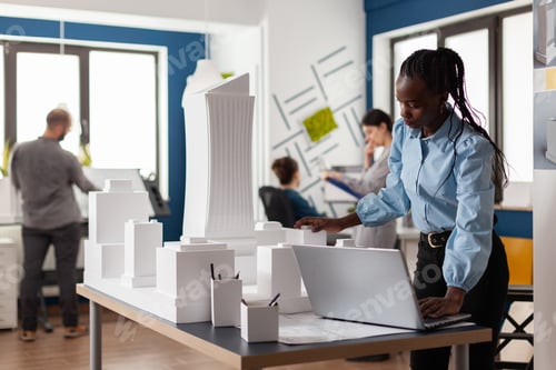 Preview: Standing architect with laptop looking at scale foam model