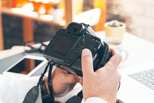 Preview: Young man photographer working on a computer. Work desk with keyboard, camera, laptop and lenses.
