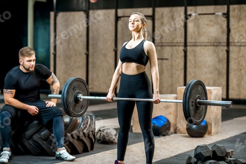 Preview: Woman lifting up a burbell with coach in the gym