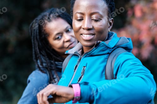Preview: Smiling black mature women monitoring smart watches outdoors in autumn.