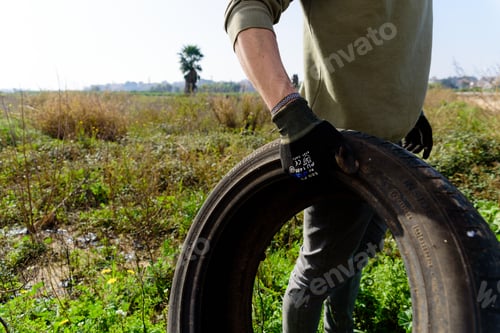 Preview: Volunteer man picks up an abandoned tire in a field during a few days of ecological cleaning.