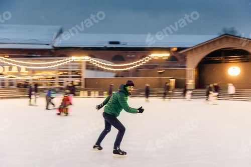Preview: Cheerful bearded man spends Christmas time on majestic ice rink decorated with lights, skates on ice