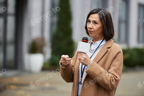 Woman in Brown Coat Speaking into Microphone Outdoors
