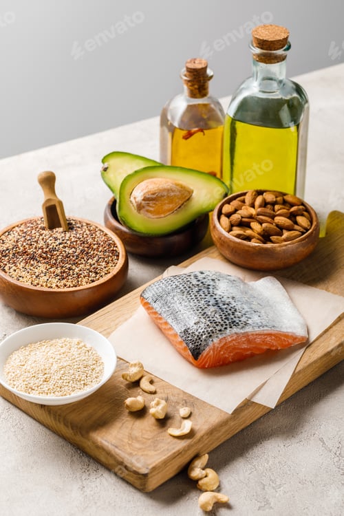 Preview: salmon, nuts, eggs and avocado on wooden chopping board near oil isolated on grey, ketogenic diet