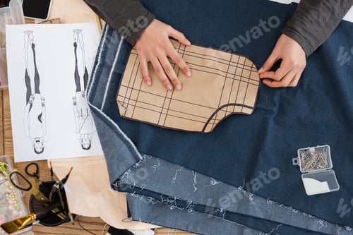 Preview: Top view of african american craftswoman holding sewing print near denim cloth and sketch in